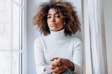 Modern beyaz pencere eşiğinde oturan düşünceli genç kadın.