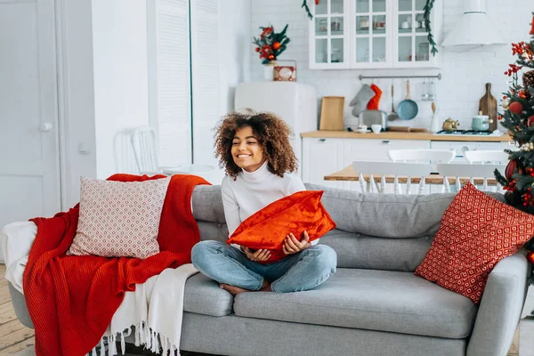 Lady holding pillow on head sits in lotus yoga pose on sofa