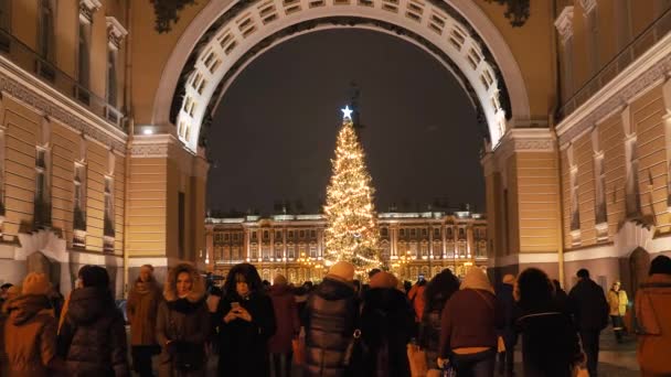 Толпы людей ходят и фотографируют на Дворцовой площади возле праздничной ели в центре Санкт-Петербурга. РОССИЯ, 26 декабря - ПЕТЕРСБУРГ. — стоковое видео