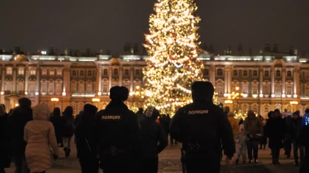 Policiais de patrulha caminham ao redor da praça do Palácio em torno da árvore de Natal entre os cidadãos celebrantes, manter a ordem. RÚSSIA, ST. PETERSBURGO, 26 de dezembro de 2020 — Vídeo de Stock