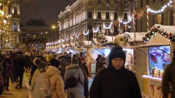 Orvosi védőmaszkos emberek sétálnak a karácsonyi piacon a város központjában egy téli estén. Oroszország, St. PETERSBURG, DECEMBER 26, 2020 — Stock videók