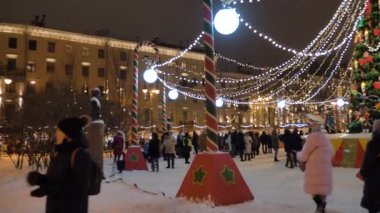 Şehir merkezindeki Noel pazarında, çelenk ve oyuncaklarla süslenmiş bir köknar ağacının yanında bir sürü insan yürüyor. Rusya, St. Peter Burgusu, 26 Aralık 2020