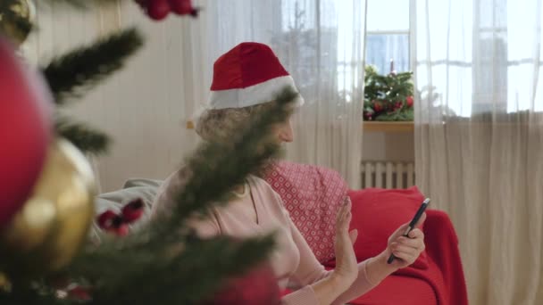 Starsza kobieta z kapeluszem Świętego Mikołaja na głowie korzysta z połączenia wideo — Wideo stockowe