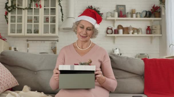 Elderly woman in hat holds box on knees and opens present — Stock Video