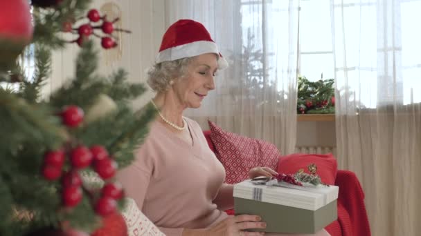Starsza kobieta w kapeluszu Santa Claus otwiera urządzone pudełko prezentów — Wideo stockowe