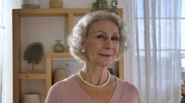 Zarif emekli kadın kameraya bakar ve nazikçe gülümser.