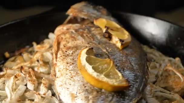 Panela com peixe dorada frito em fatias de cebola e limão em cima — Vídeo de Stock