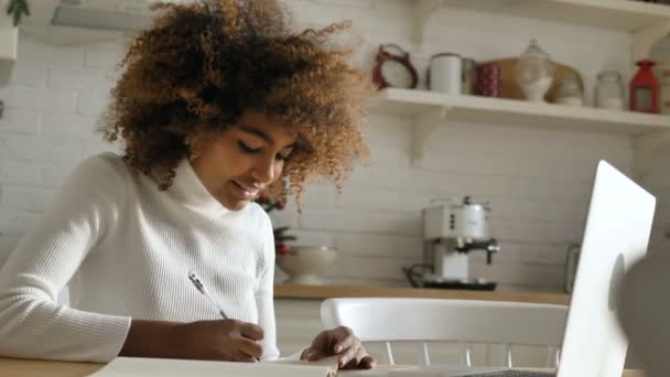 Estudante senta-se contra notebook escreve notas no pad em casa — Vídeo de Stock