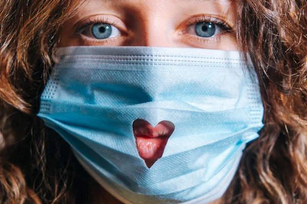 Красива жінка з блакитними очима в медичній масці з відрізаним серцем дивиться в камеру крупним планом, концепцію Валентинів день. — стокове фото