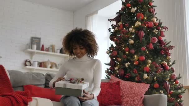 Tmavá žena drží krabici na kolenou a otevírá dárek — Stock video