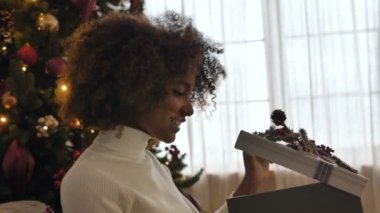 Koyu tenli hoş bir bayan hediye kutusunu açar ve geniş bir gülümseme sergiler.