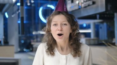 Kafasında koni olan kadın kameraya el çırpıyor ve gülümsüyor.