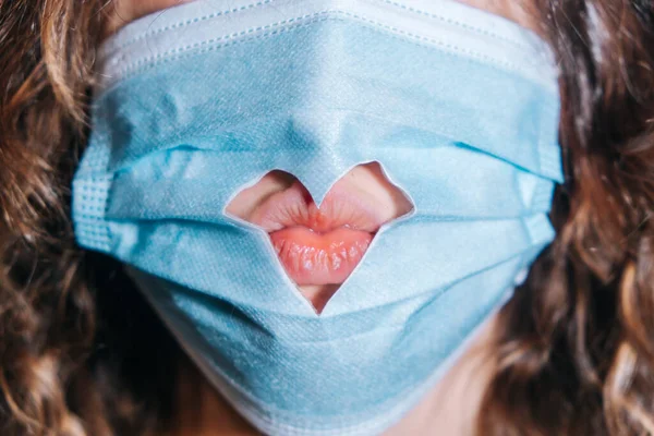 Медицинская маска на лице девушки с вырезанным сердцем крупным планом и женскими губами, празднование Дня Святого Валентина — стоковое фото