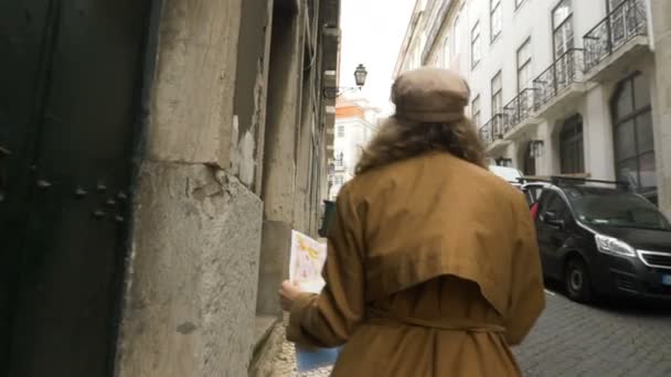 Turista barna kabátban sétál keskeny európai utcákon térképpel — Stock videók