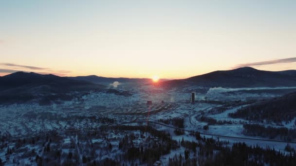 Ciudad y planta con chimenea en valle nevado cerca de montañas — Vídeos de Stock