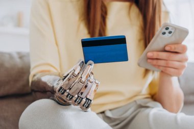 Protez kollu bir kadın kredi kartı ve telefonu koltukta tutuyor.