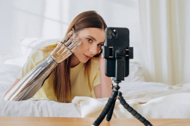 Sarışın kadın biyonik kolu yatakta blog için kameraya gösteriyor.