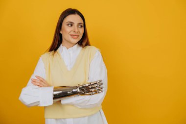 Biyonik protezi olan kadın sarı duvarla kollarını kavuşturuyor.