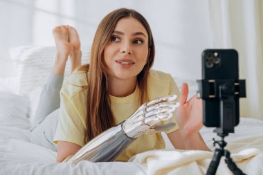 Biyonik protez kollu bir kadın blogcu bir internet yayınını yönetiyor ya da bir konuyu kaydediyor ya da yatakta uzanırken arkadaşlarıyla görüntülü iletişim kuruyor.