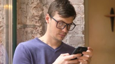 Gözlüklü genç adam akıllı telefonu tutuyor ve bilgi okuyor.