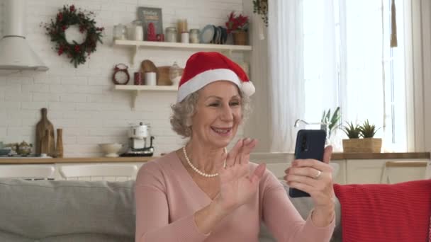 Kırmızı şapkalı neşeli yaşlı kadın gülümsüyor ve video çağrısı yapıyor. — Stok video