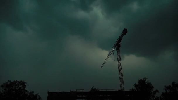 Konstruktion kran och oavslutade flervåningshus mot bakgrund av mörkt regn moln, blixtar, slow motion — Stockvideo