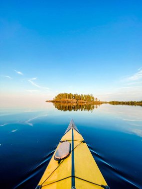 Sarı kanonun burnu, sakin mavi gölün üzerinde ufuktaki adaya doğru süzülüyor, macera ve açık hava aktiviteleri.