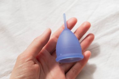 Kadın avuç içi, beyaz bir çarşafın arkasında regl bardağı tutuyor.