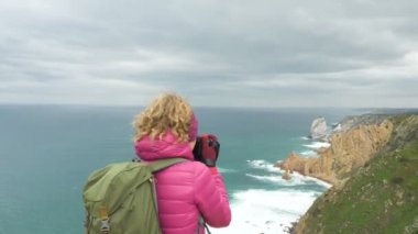 Pembe ceketli turist kötü bir günde okyanusun resmini çeker.