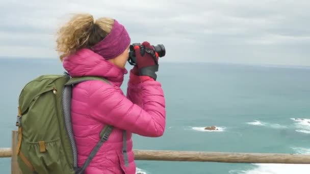 Turista en chaqueta rosa toma foto del océano en día desagradable — Vídeos de Stock