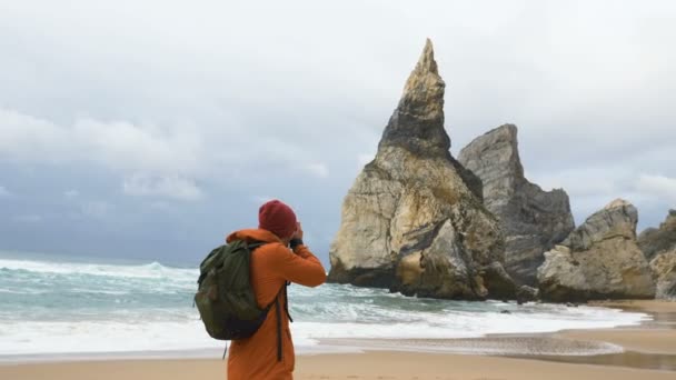Joven toma fotos contra acantilado empinado en la playa del mar — Vídeos de Stock