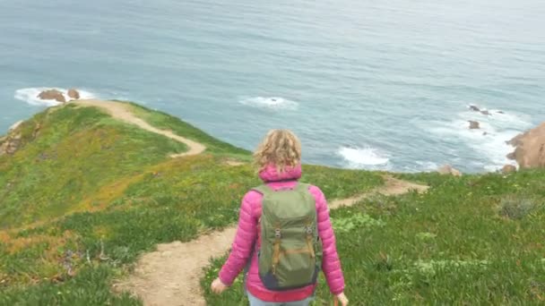 Дівчина в рожевій куртці ходить уздовж океанського узбережжя в неприємний день — стокове відео