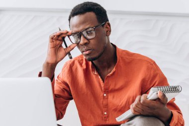 Kalem ve not defteri olan Afro-Amerikalı bir adam dizüstü bilgisayara bakar.