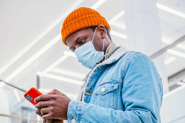 Афроамериканець у масці використовує мобільний телефон у коридорі. — стокове фото