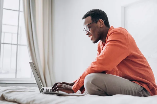 African-American man freelancer works on laptop on bed