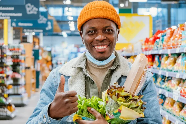 Улыбающийся афроамериканец показывает большой палец, держа салаты — стоковое фото