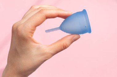 Lady hand shows menstrual cup on pink color background