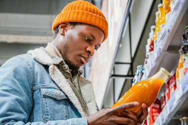 Düşünceli siyah adam süpermarkette meyve suyu şişesine bakıyor.