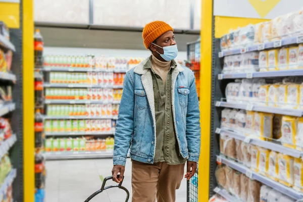 Афроамериканец в маске проходит мимо полок в магазине — стоковое фото