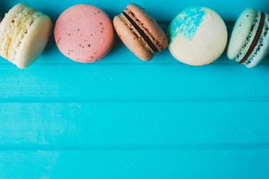 Turkuaz ahşap arka planda çok renkli taze bademli kurabiyeler, yakın plan. Boşluğu kopyala