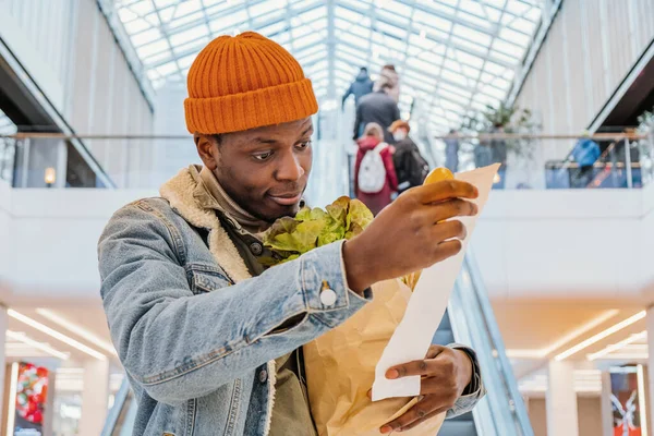Удивленный черный мужчина смотрит на квитанцию с едой в торговом центре — стоковое фото