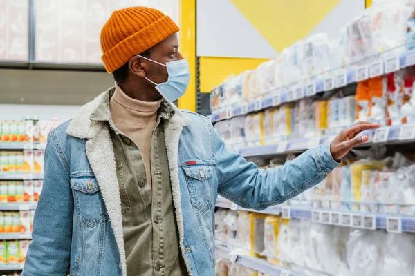 Афроамериканец в маске выбирает товары в супермаркете — стоковое фото