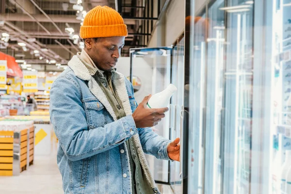 Афроамериканец берет молоко из холодильника в супермаркете — стоковое фото