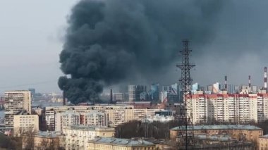 Yakın planda büyük bir yangın, kalın siyah bir duman sütunu şehrin arka planına doğru yükseliyor.
