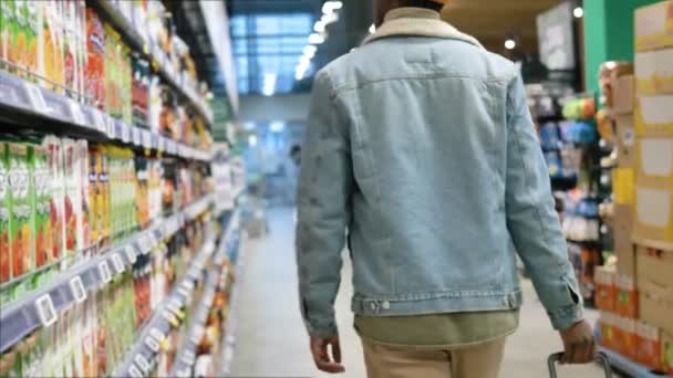 Черный покупатель в куртке бродит по длинному продуктовому магазину — стоковое видео
