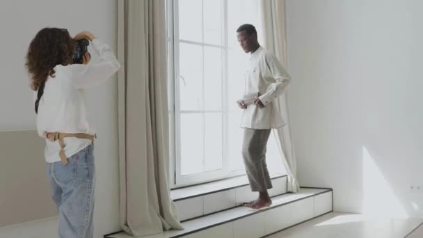 Счастливый афроамериканец позирует для женщины у окна — стоковое видео