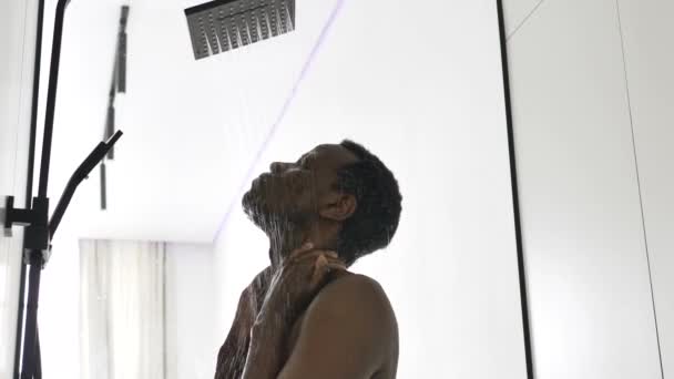 Hombre afroamericano toma ducha caliente en baño ligero — Vídeos de Stock