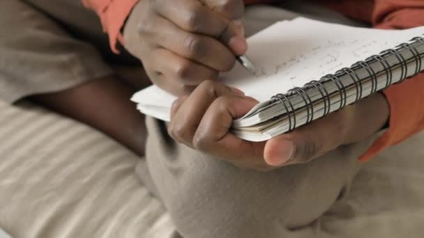 African-American man writes in notebook sitting on soft bed — Stock Video