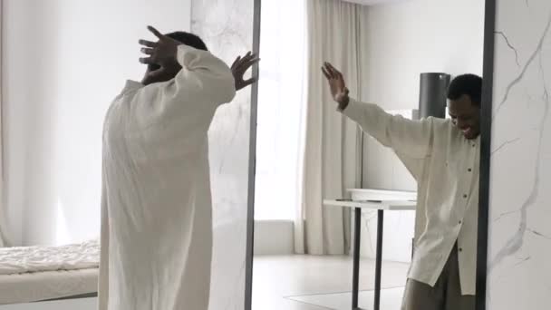 Позитивный афроамериканец в футболках танцует возле зеркала — стоковое видео