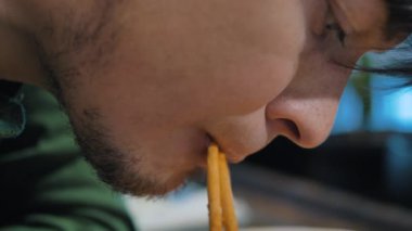 Süveter giyen kısa sakallı genç adam kaseden erişte yiyor.